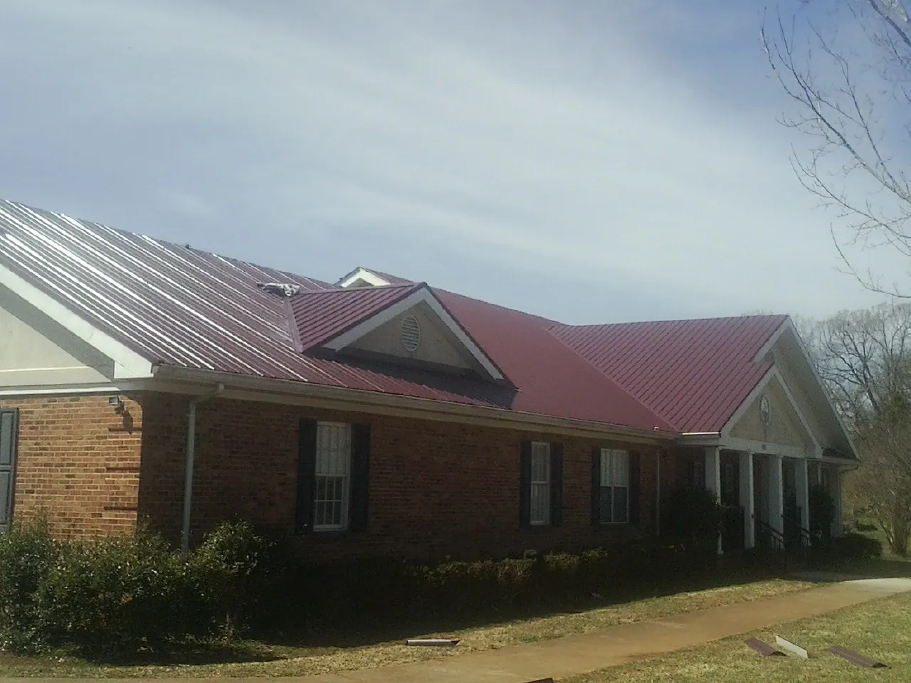 Red metal roof with gabled entries on a long brick building, from a Hail Damage Roof Repair job in Sligo