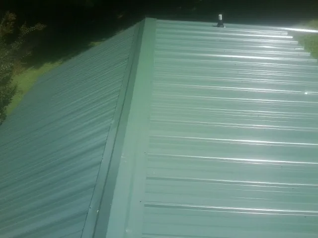 New green metal panels meeting at the ridge of a roof — Flat Roof Repair work by our crew in Sligo