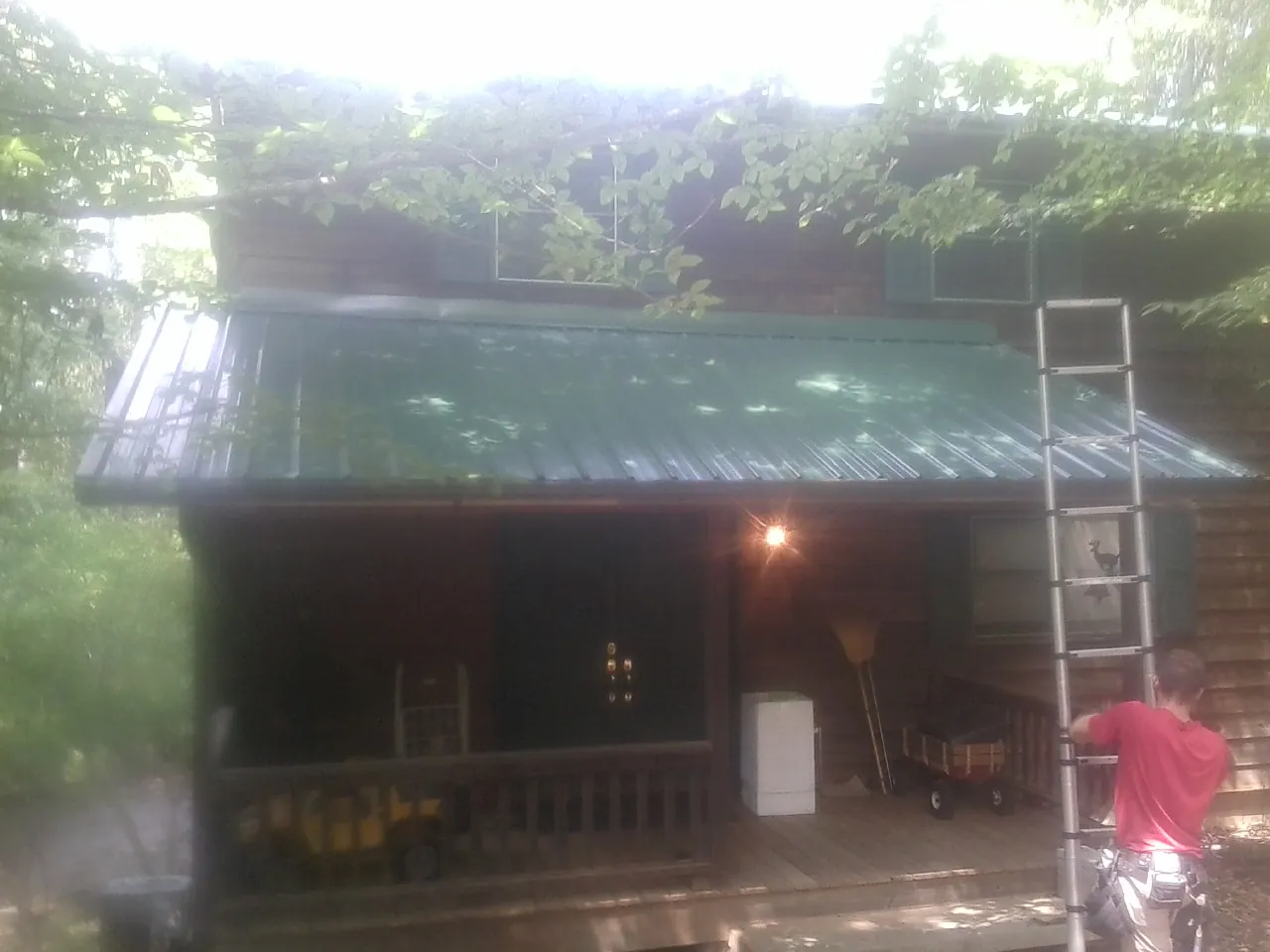 Worker on a ladder at the green porch roof of a wooded cabin in Sligo