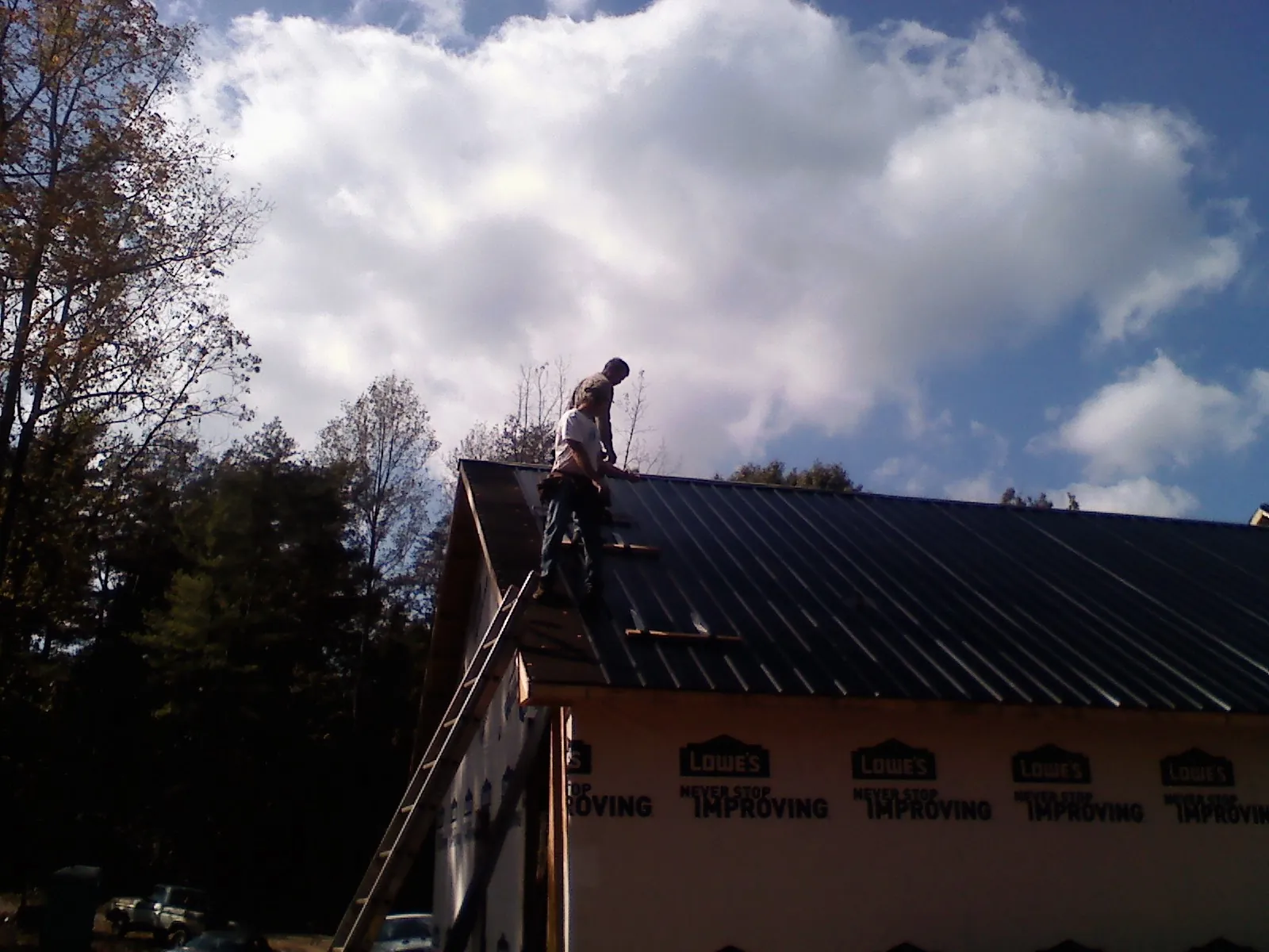 Roofer fastening dark metal panels high against a cloudy sky, from a Roof Inspection job in Sligo