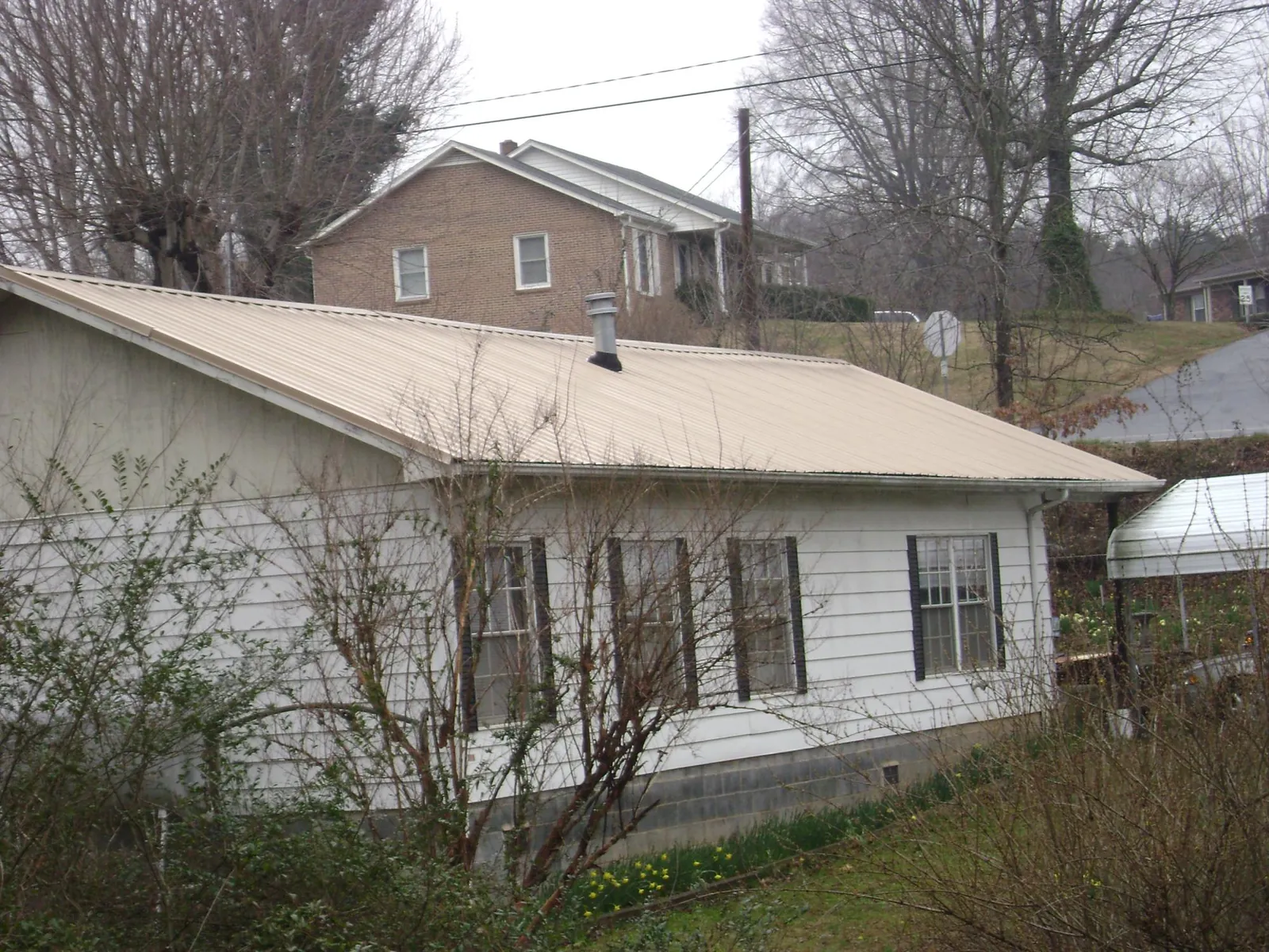 Tan metal roof on a white sided house set into a hillside — Commercial Roofing by Roofing Brothers in Sligo